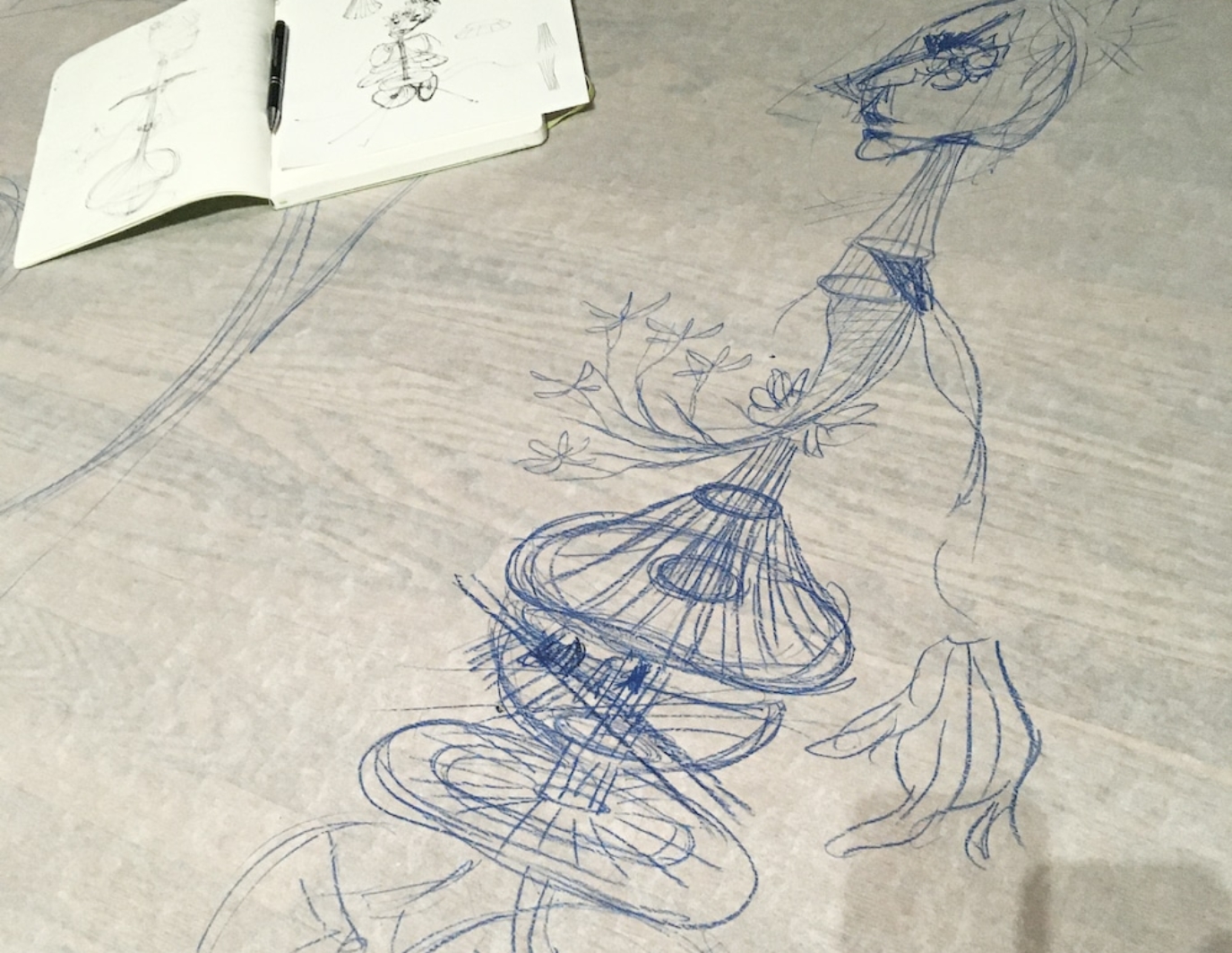 A preliminary sketch of the Dream Puppet in blue ink, on white-gray paper. There is a notebook in the top left corner with the initial sketch.