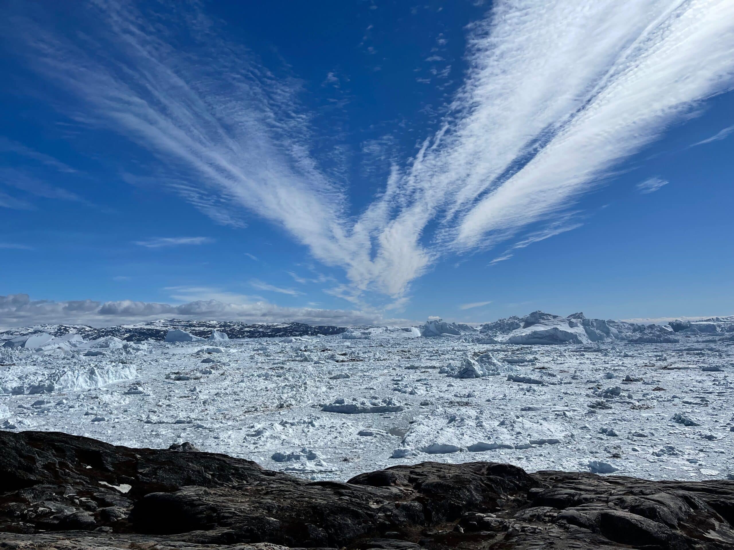 Clouds streaking across a blue sky above icy ground