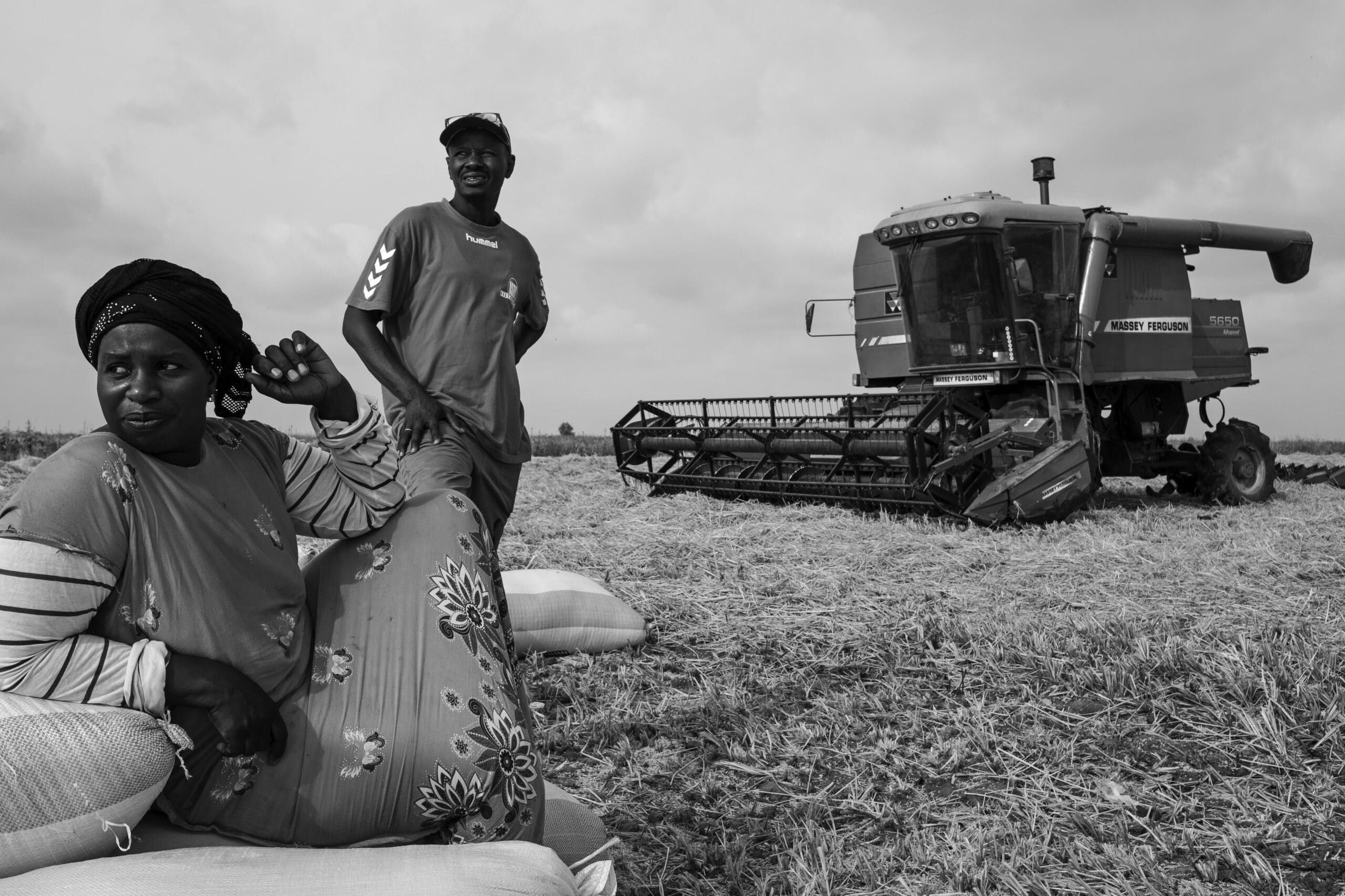 A black and white photo of a man and a woman in front of a harvesting machine 