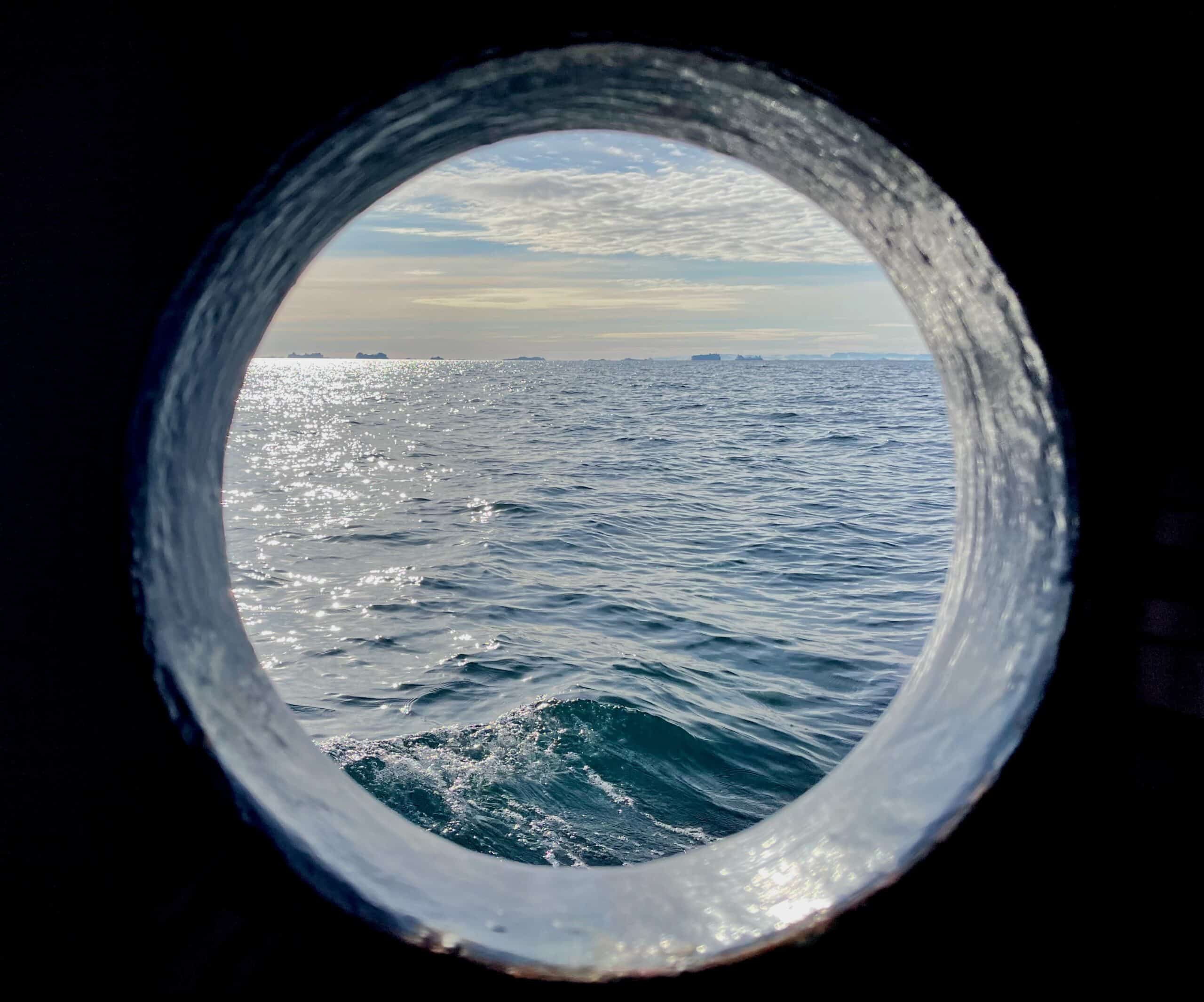 Water, sky, and clouds as seen through a circular porthole