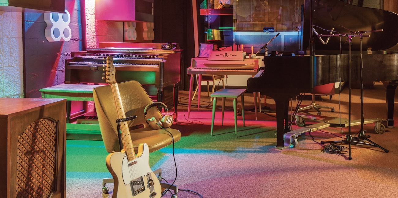 A multicolored music studio with pink and green and black. There are instruments leaning on stands and various studio furniture