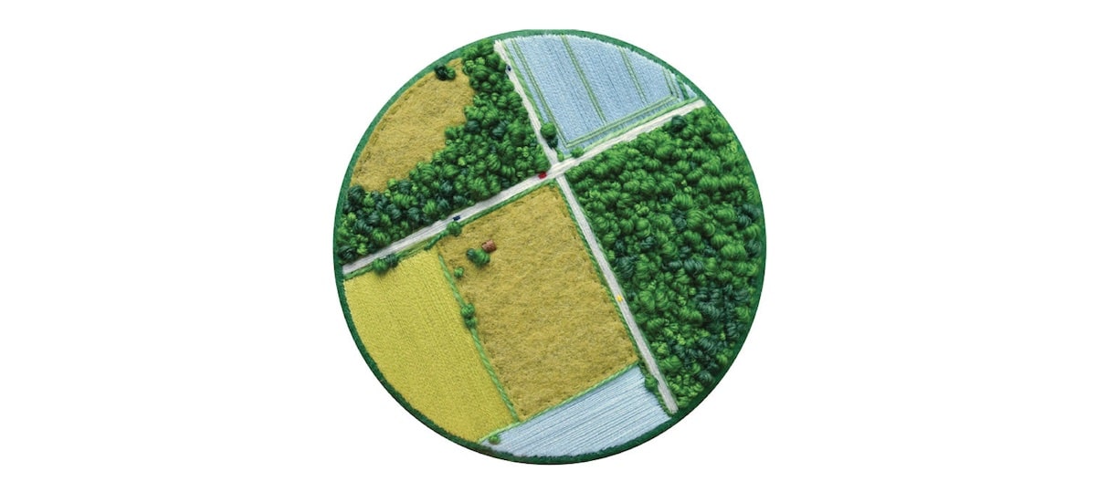 A hand-stitched aerial piece of work that appears as two road intersecting in agricultural fields of green and yellow and blue.