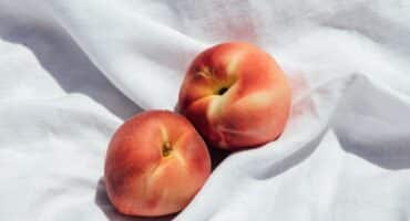 two peaches sit close on a white fabric background