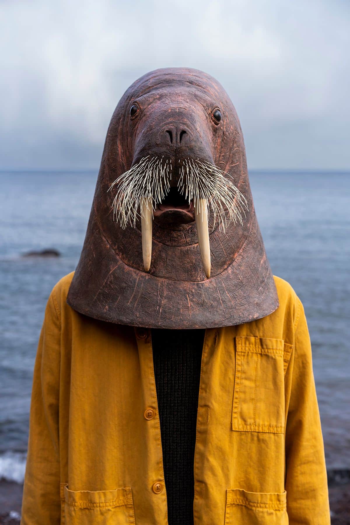 A close up photo of a person in a yellow coat wearing a walrus head over their head