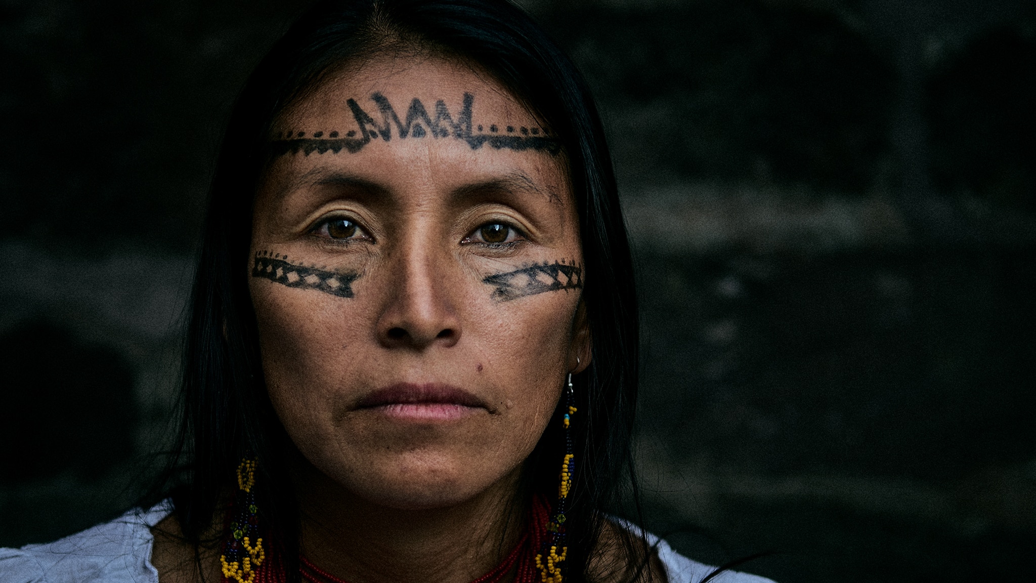 A close-up image of Salome Aranda. She is an Indigenous woman with painted markings on her face. She wears beaded earrings and a white shirt.