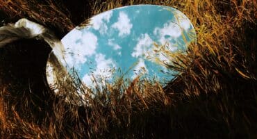 A mirror sits in tall grass, reflecting the sky above it