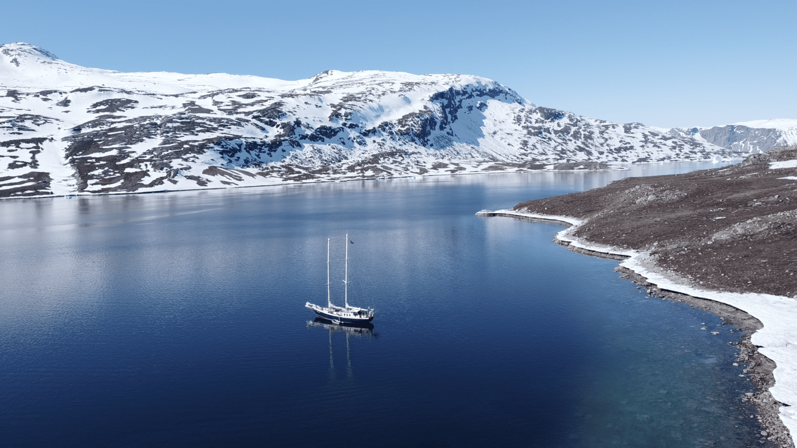 A boat on a blue water surrounded by snowy gray land.